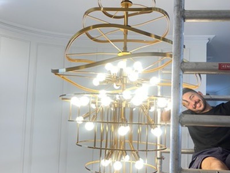 BHT crew member fitting a large brass tiered chandelier from scaffolding